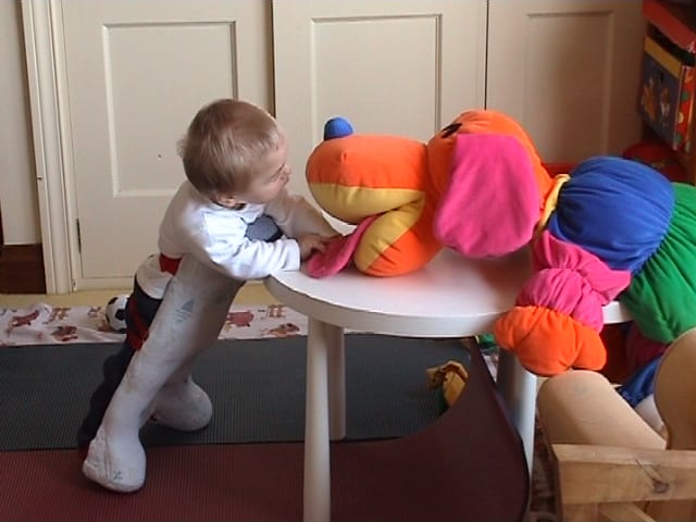A child standing with standing supports plays on a table at hand height