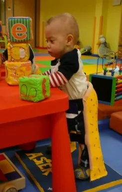 A small child plays with blocks on a table while standing in his stander