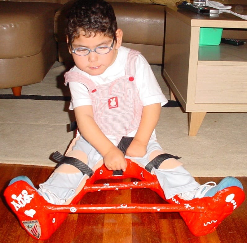 A child in a sledge-type floor seat with knee straps keeping the legs extended