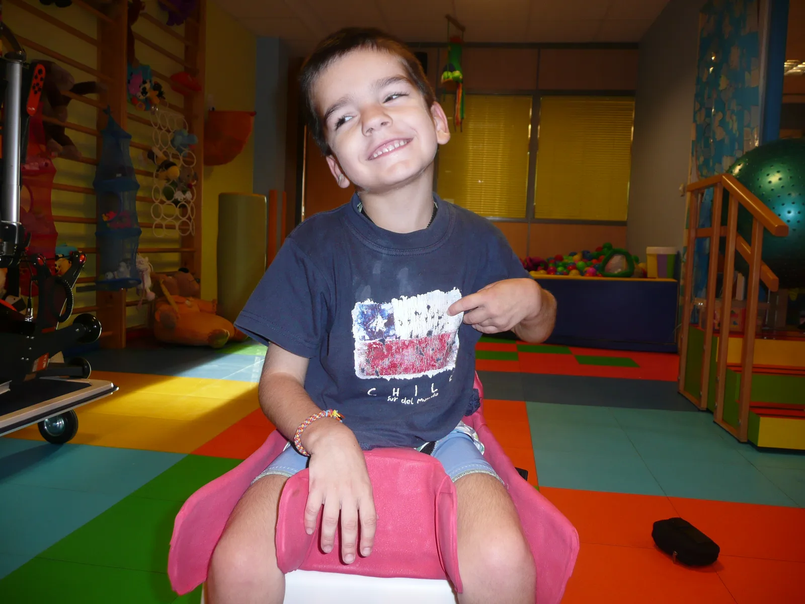 A boy smiles seated in his custom-moulded pelvic seat, in the clinic room