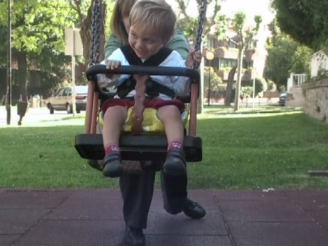 A child swings in the park seated in an adapted postural seat