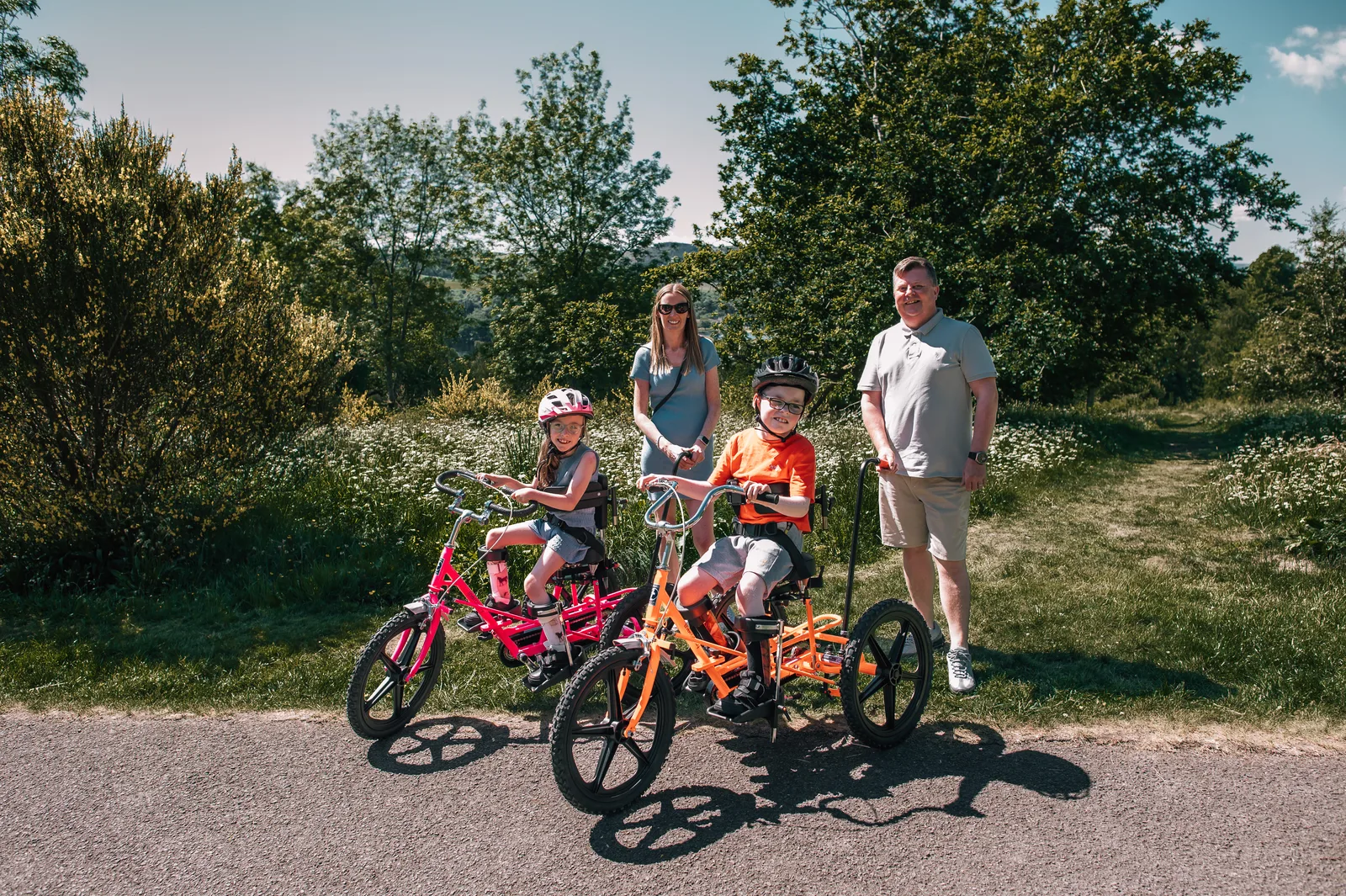 Two families walk through a park with their adapted tricycles
