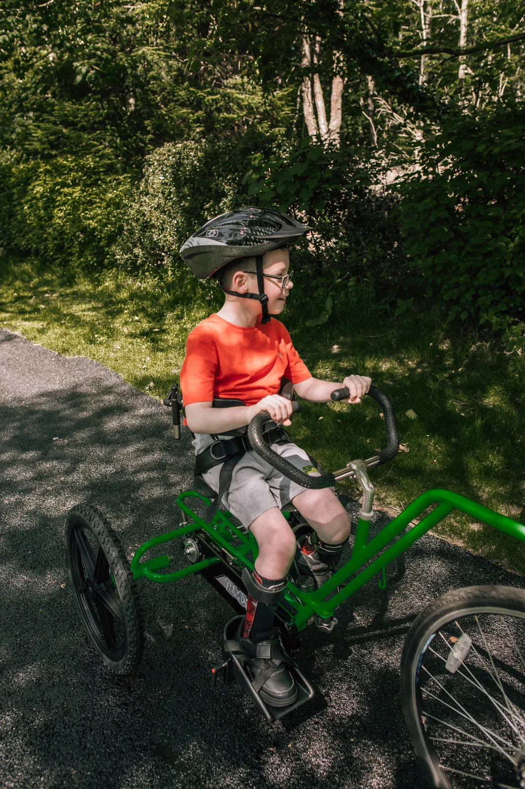 A teenager pedals a green-framed adapted tricycle